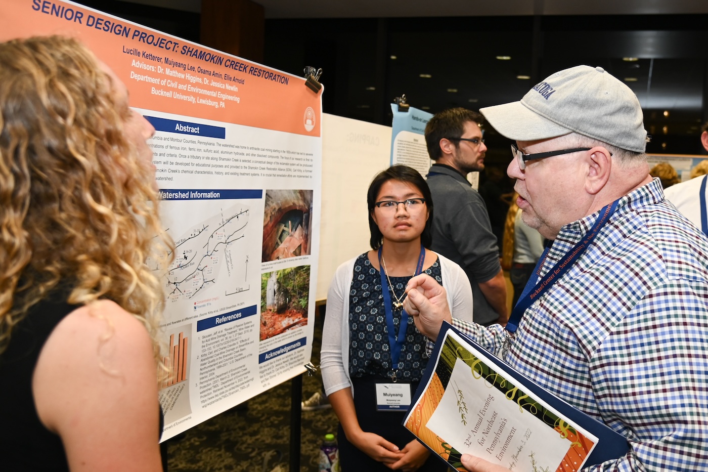 People standing around an academic poster, one presenting and several listening.